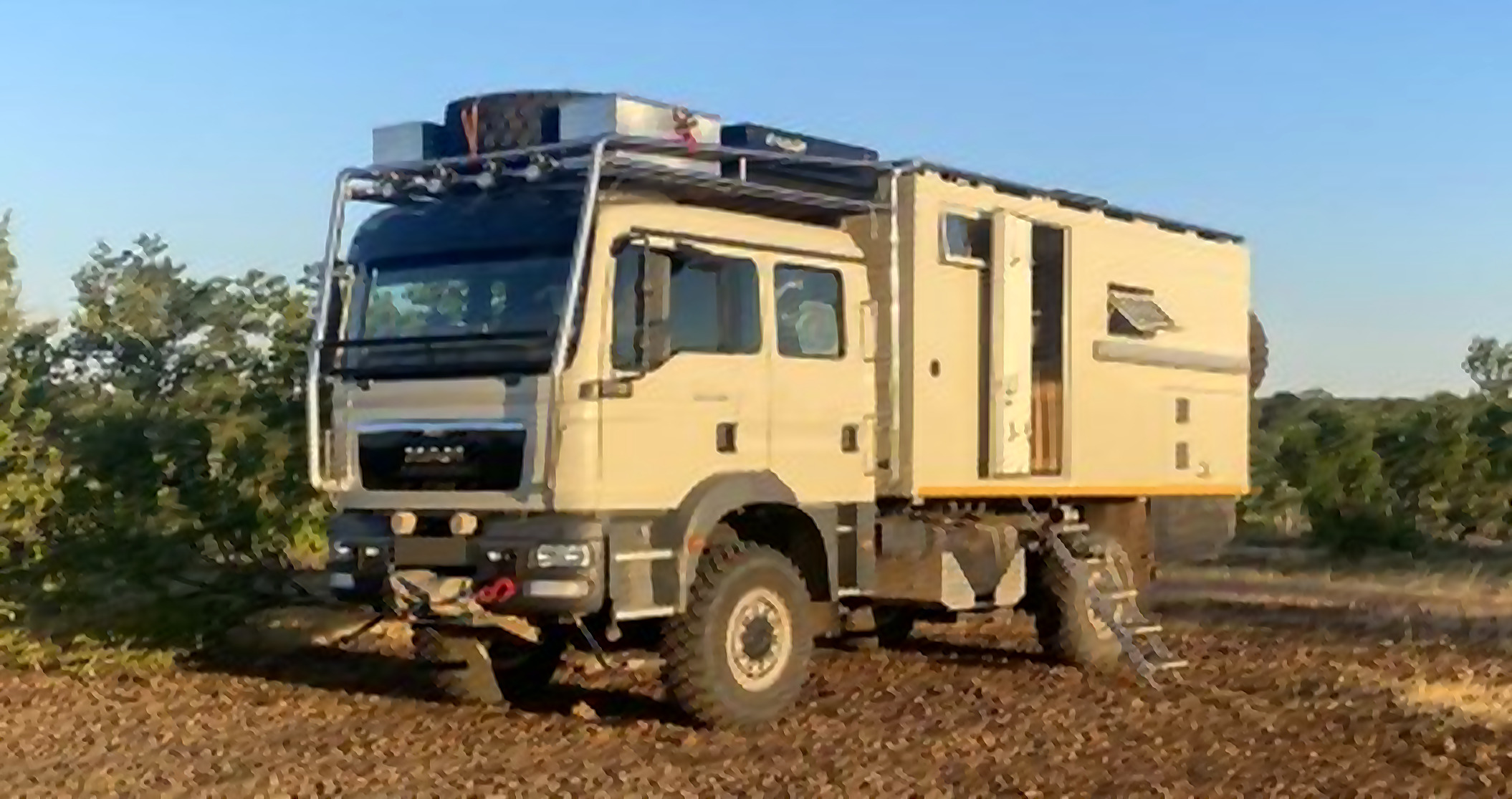 MAN TGM 4x4 cabine jour avec cellule habitable expédition, stationné en terrain rocailleux à la lumière dorée de fin de journée — le camion visé pour le projet.